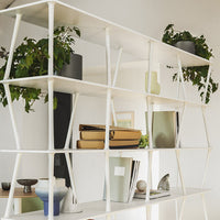 White geometric shelving unit with various plant pots, neutral decor items, and a minimalist design.