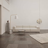 Beige sofa with ribbed texture, light gray walls, dark gray flooring, and neutral-toned area rug. Modern minimalist style.