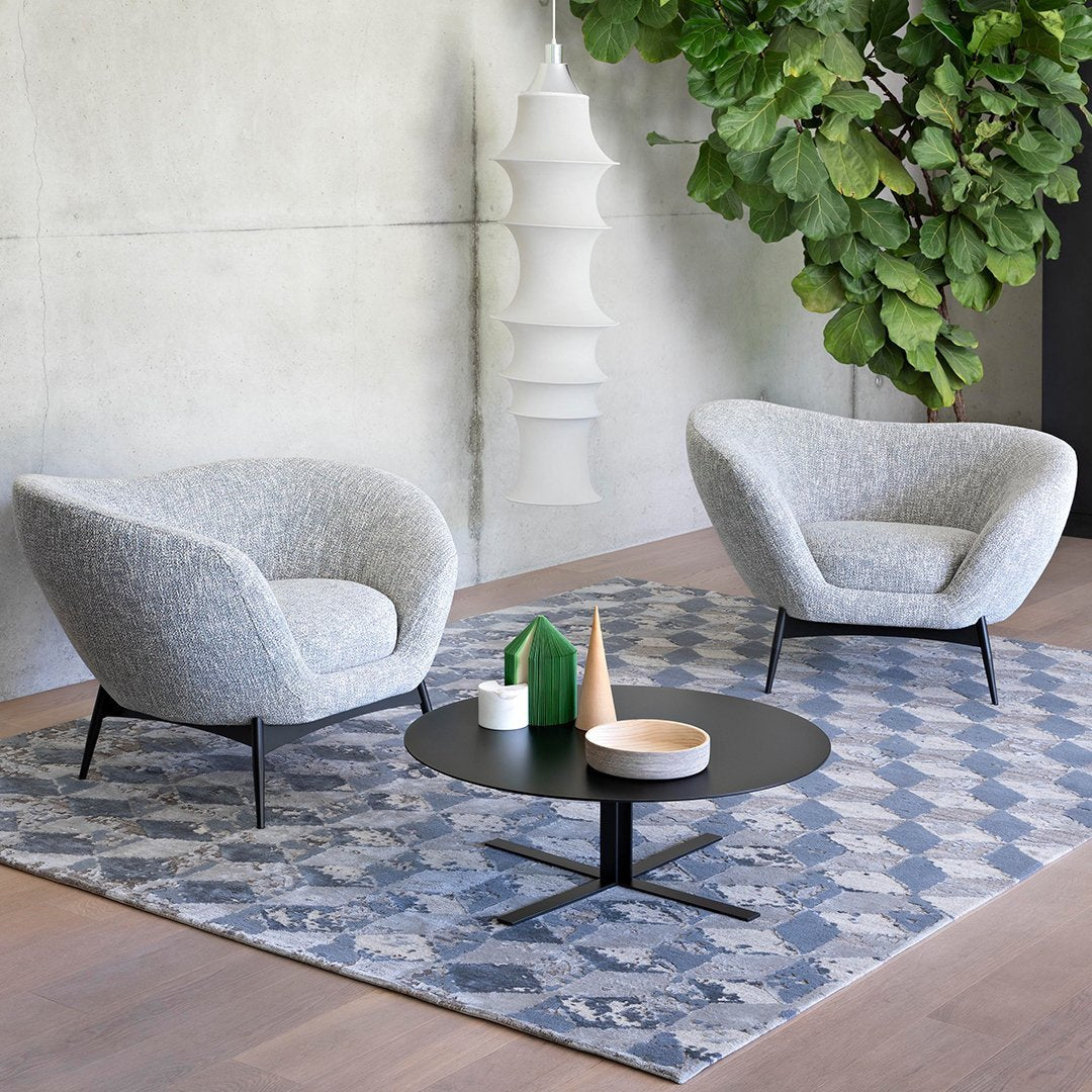 "Gray textured armchairs on a geometric blue and white rug with a black coffee table, accented by green decor."