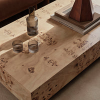 Natural wood coffee table with light beige tones and unique dark burled patterns. Glassware and decor accentuate the design.