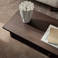 Dark wood coffee table with smooth surface, accompanied by a white textured vase and beige book on a soft carpet.
