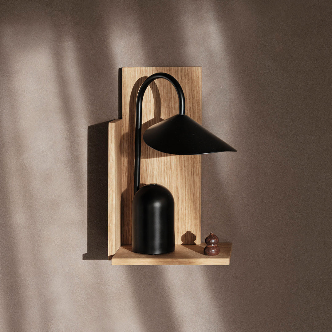 Black metal lamp with a smooth finish, mounted on a light wooden backdrop, casting soft shadows.