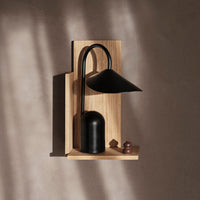 Black metal lamp with a smooth finish, mounted on a light wooden backdrop, casting soft shadows.