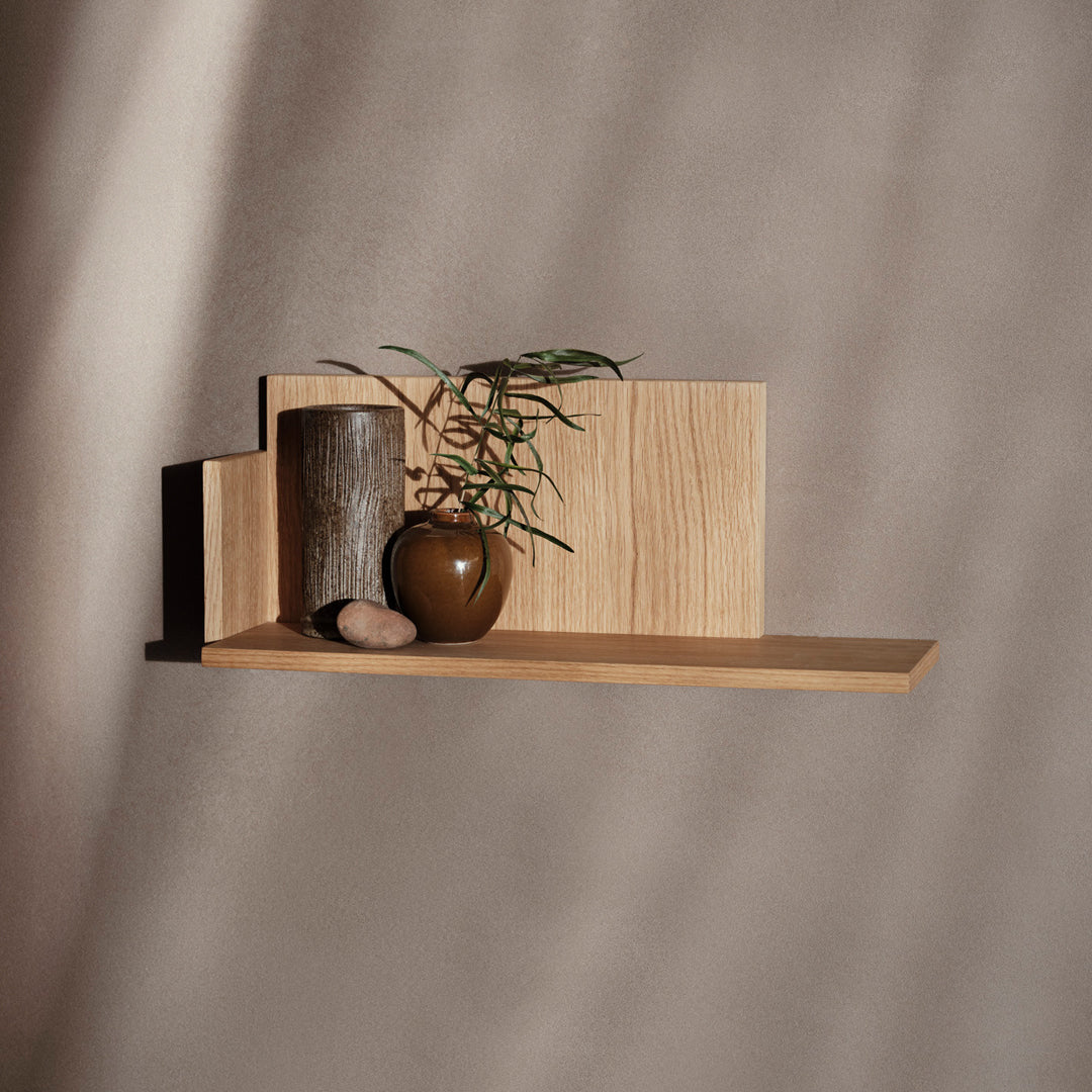 Wooden shelf with light oak finish, featuring earthy tones and natural textures, complemented by a dark ceramic vase and greenery.
