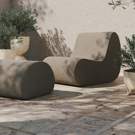 "Modern furniture in soft beige tones with smooth, rounded shapes against a textured stone background."