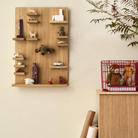 Wooden display shelf in natural oak with colorful decorative items and a red wire basket, featuring earthy tones and geometric shapes.
