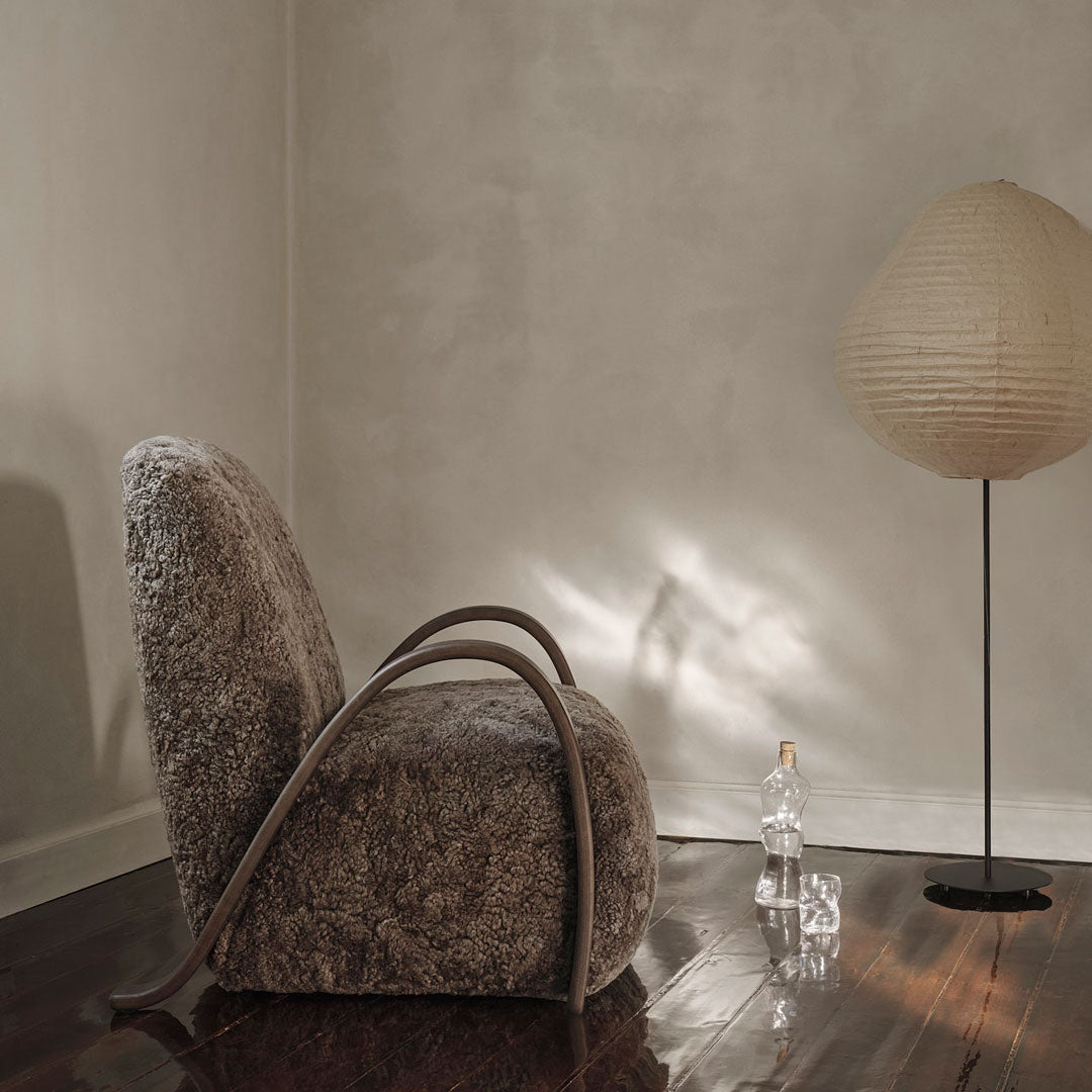 Textured brown chair with curved wooden arms, complemented by a neutral setting and soft, warm lighting.