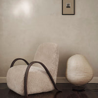 "Textured cream armchair with curved wooden arms, paired with a soft white lamp against a neutral wall."