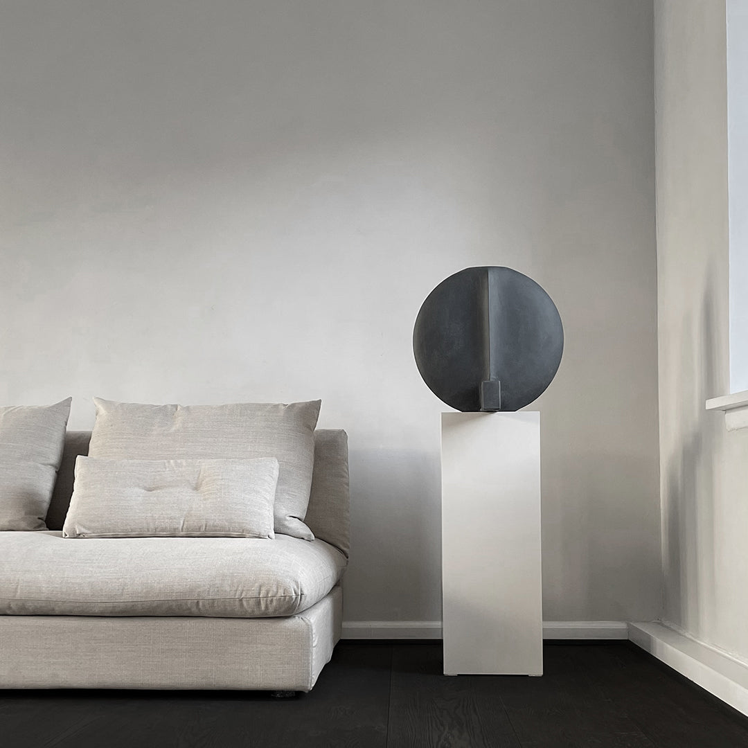 "Minimalist gray and white decor featuring a round black sculpture on a sleek white pedestal."