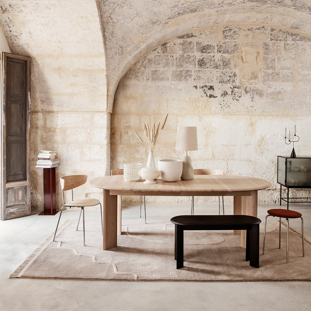 Light wood dining table with a smooth finish, complemented by neutral cream tones and subtle geometric patterns in the rug.