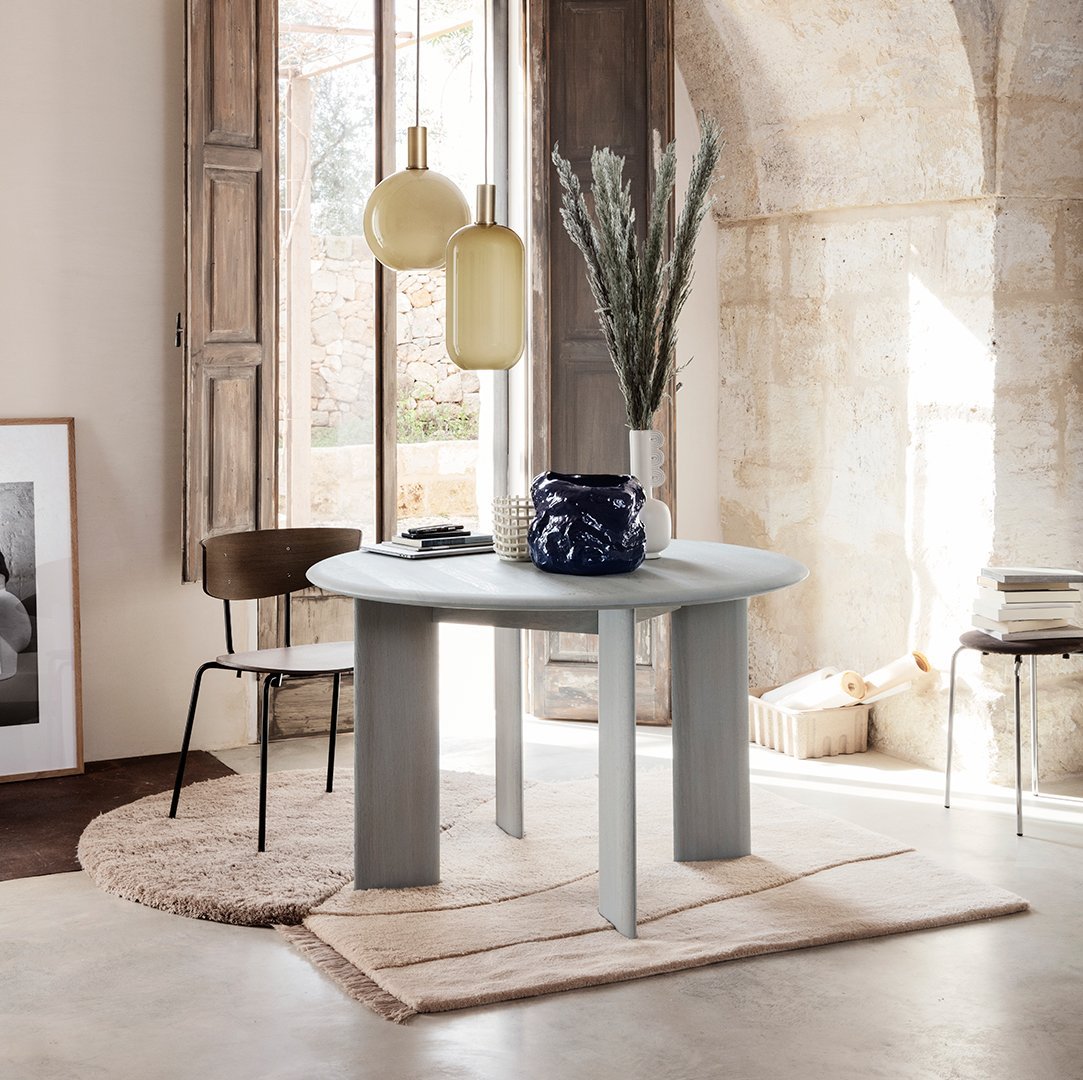 Round gray dining table with smooth texture, complemented by earthy tones and minimalist decor in a bright, airy setting.