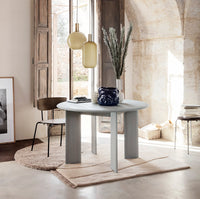 Round gray dining table with smooth texture, complemented by earthy tones and minimalist decor in a bright, airy setting.