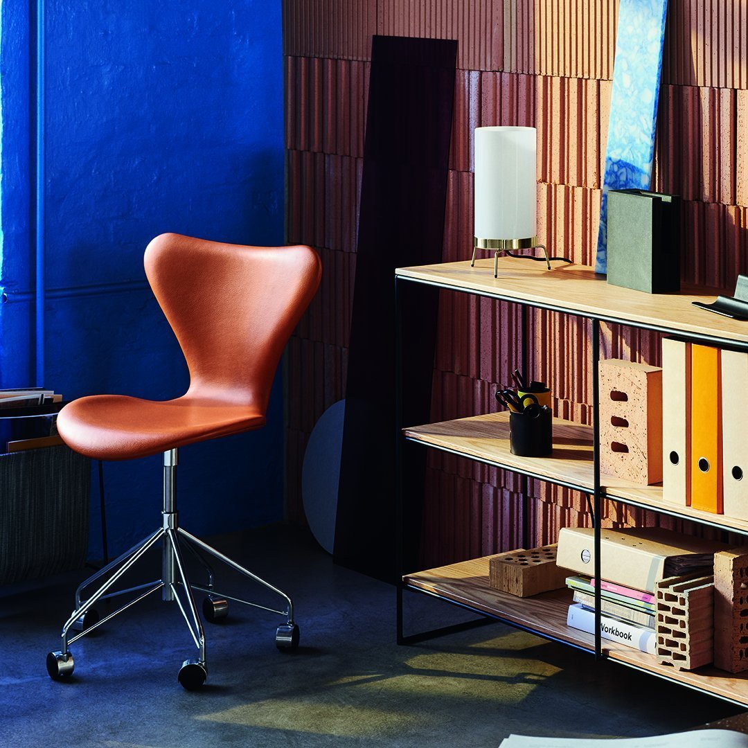 Brown swivel chair against a blue wall and patterned wood paneling, with stylish shelving displaying office supplies.