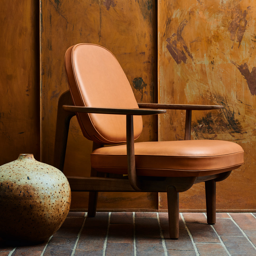 "Mid-century modern chair in warm terracotta leather, with a smooth finish against a rustic, textured backdrop."