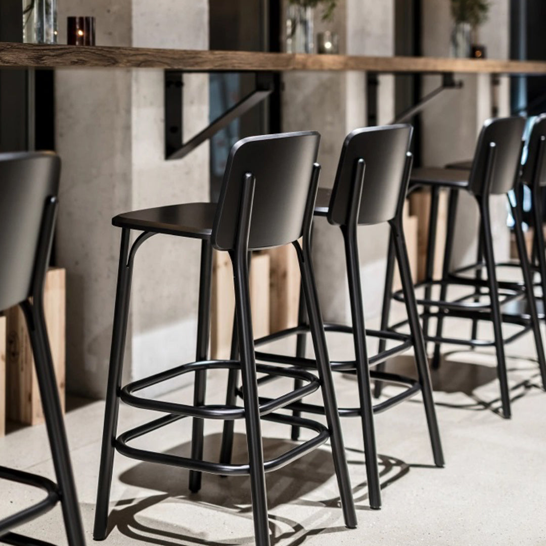 Black metal bar stools lined up against a concrete wall, showcasing sleek, modern design and minimalist aesthetic.