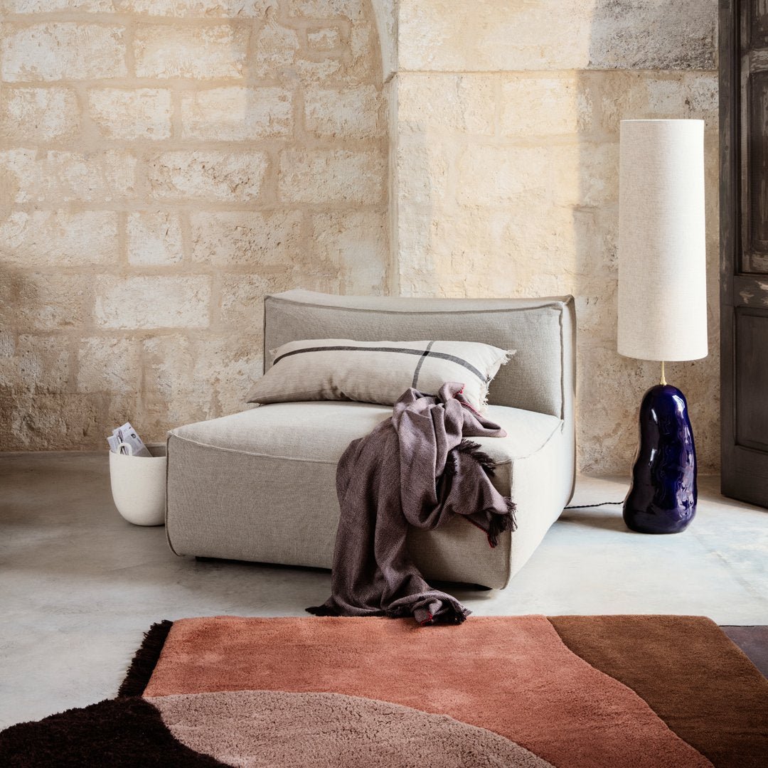 Soft gray modular chair with a cozy purple throw, complemented by a round brown and pink patterned rug.
