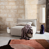 Soft gray modular chair with a cozy purple throw, complemented by a round brown and pink patterned rug.