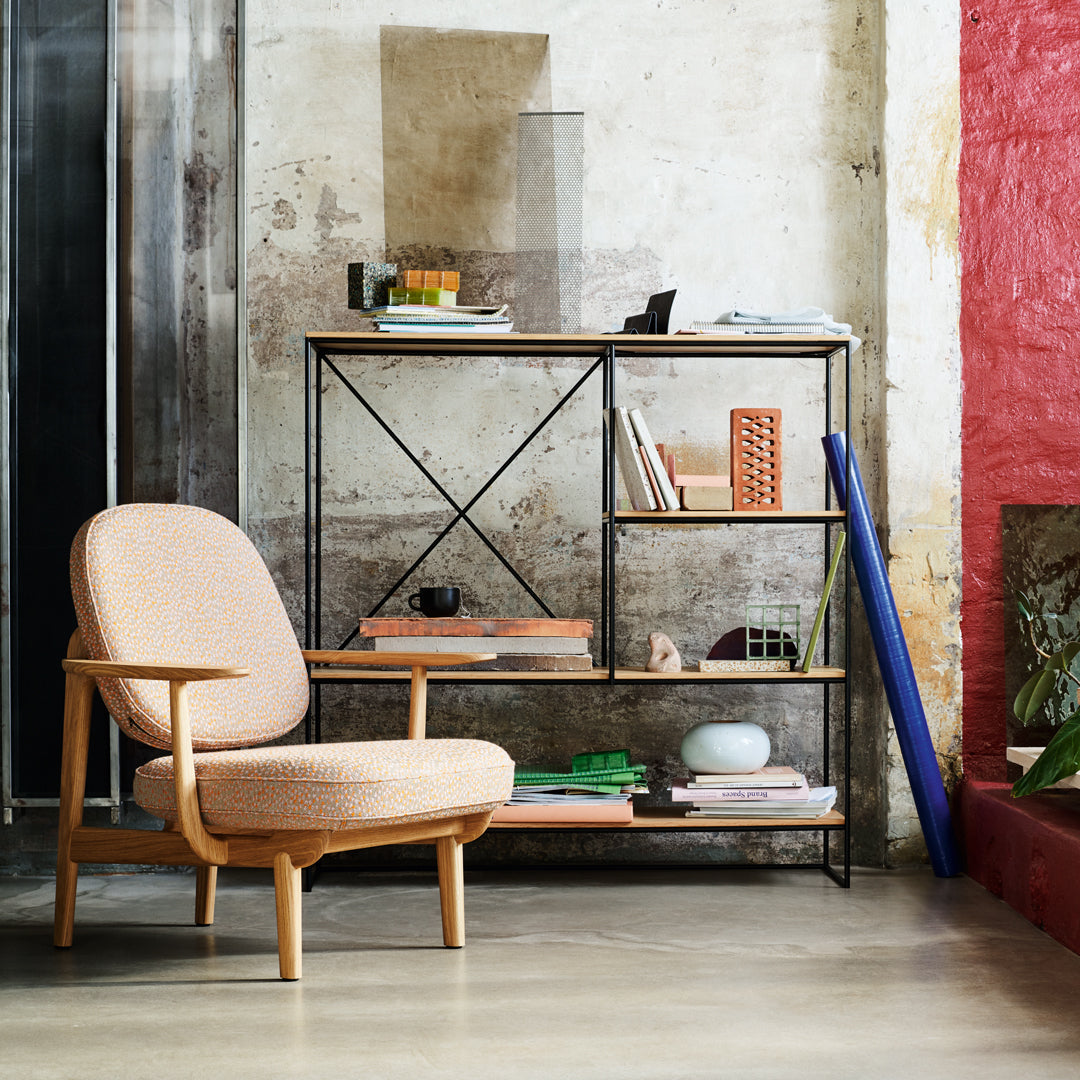 Light brown upholstered chair with a simple pattern, black metal shelving unit, and vibrant red wall accents.