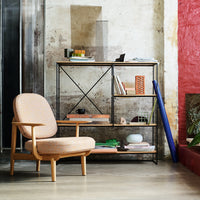 "Beige upholstered chair and black metal shelving against textured walls in red and neutral tones with vibrant decor accents."