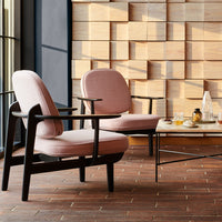 "Two pink armchairs with black frames in a chic interior, complemented by a modern glass coffee table and wooden backdrop."