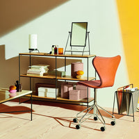 Modern wooden shelving unit with black metal frame, rust-colored chair, and pastel-colored decor on a warm yellow backdrop.