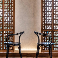 "Black wooden chairs against a textured beige wall and intricate patterned wooden screen."