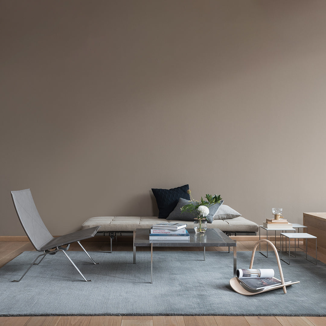 Modern living room featuring a light gray rug, sleek glass tables, and muted blue and green accents on cushions.