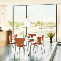 "Modern dining set with warm orange chairs, sleek white table, and soft, natural light from large windows."