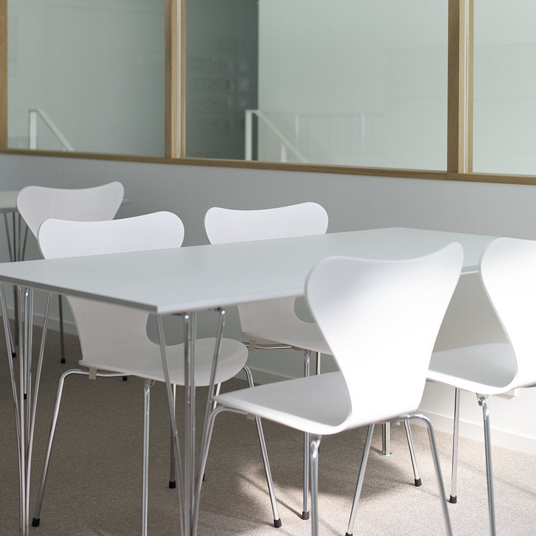 White modern dining table with four matching minimalistic chairs against a light backdrop.