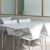 White modern dining table with four matching minimalistic chairs against a light backdrop.