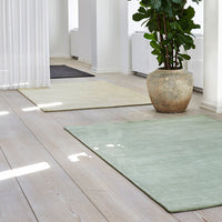 Soft green, pale yellow, and dark gray rugs with a textured surface, set on light wooden flooring.