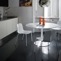 Modern white dining set with round table and sleek chairs, contrasting against a dark floor and minimalist decor.
