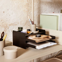 Black wooden organizer with white and beige papers, green and grey accents, and ceramic desk accessories. 