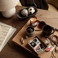 Round black and white decorative balls, amber candle, earthy tones, and mixed patterns on a wooden tray.