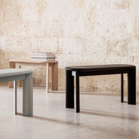 Minimalist tables in light gray, natural wood, and deep black finishes, featuring smooth lines and elegant shapes.