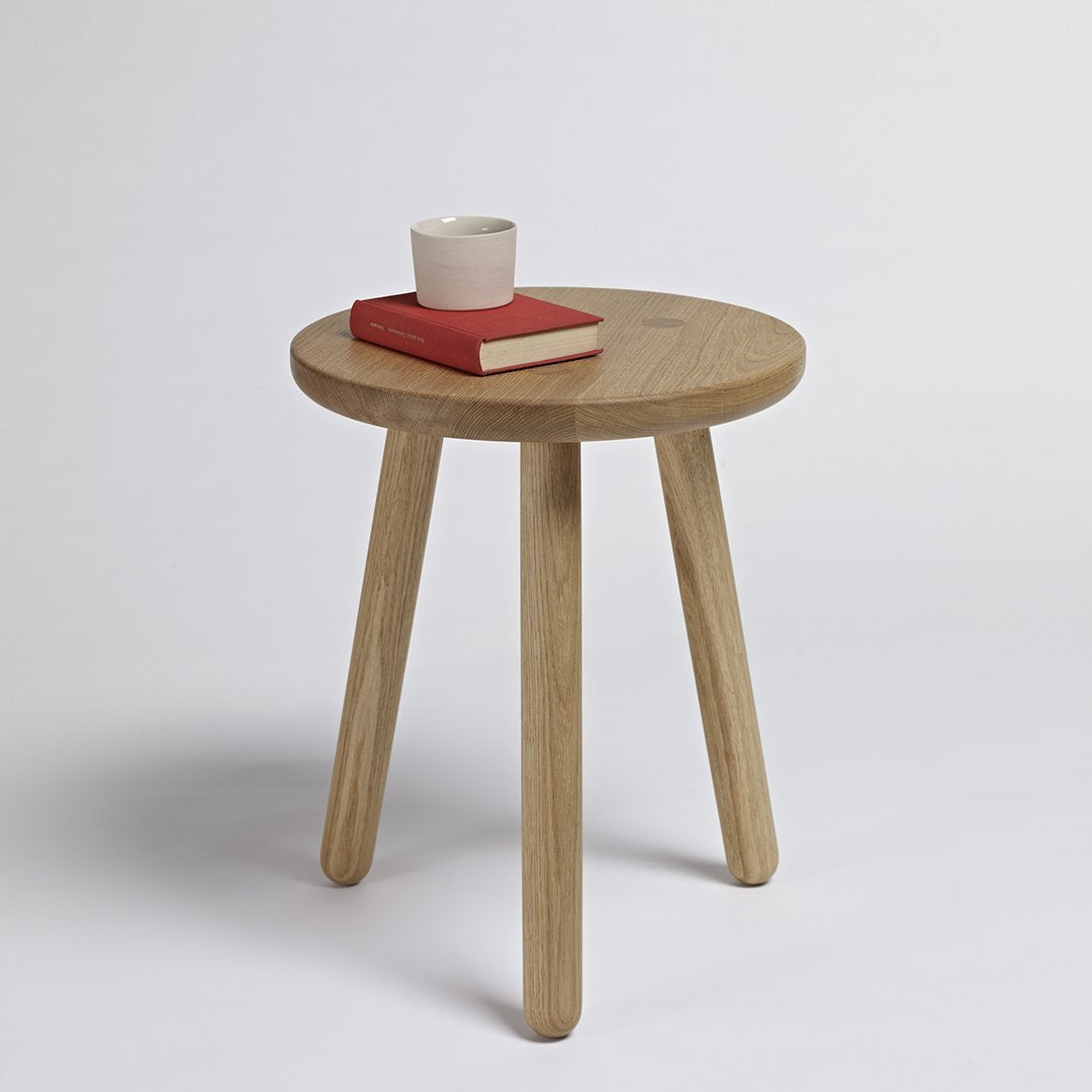 Natural wood round side table with three light wooden legs, styled with a white cup and red book.