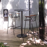 Black metal bar table with geometric wire stools featuring wooden accents, set against a natural wood deck.