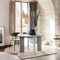 Round gray table with light wood accents, soft beige rug, and blue patterned vase, set in a bright, rustic room.