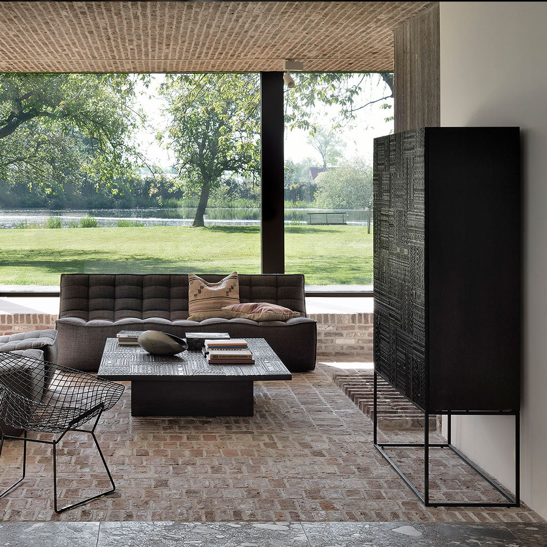 Modern living room featuring a black cabinet, gray furniture, and earthy tones, with a natural pattern of greenery outside.