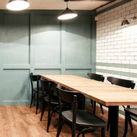 "Stylish dining area featuring muted teal walls, rustic wood table, and black chairs against a white brick backdrop."