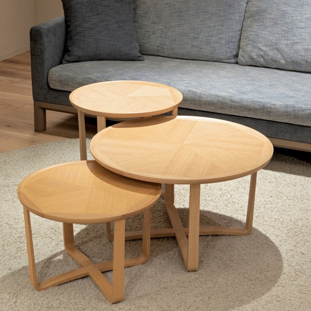Set of three round wooden nesting tables in light oak finish with natural grain pattern, complementing a gray sofa.