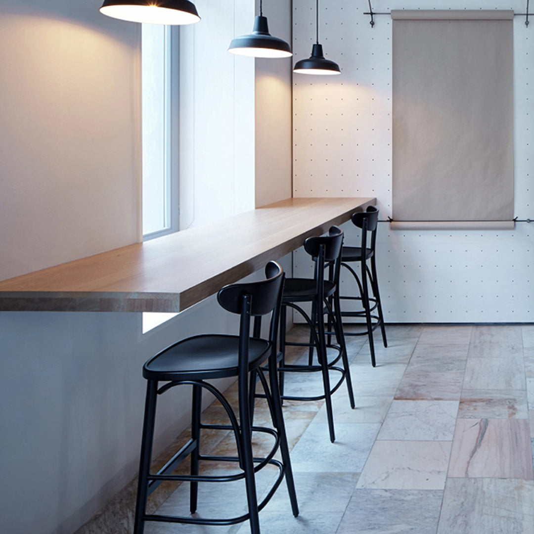 Black bar stools with minimalist design against a wooden countertop and neutral walls, featuring soft lighting.