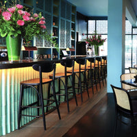 "Chic bar stools in black, surrounded by vibrant green accents and floral arrangements against a light blue backdrop."