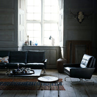 "Modern black leather sofa and armchair, featuring a textured area rug in warm tones against a soft gray backdrop."