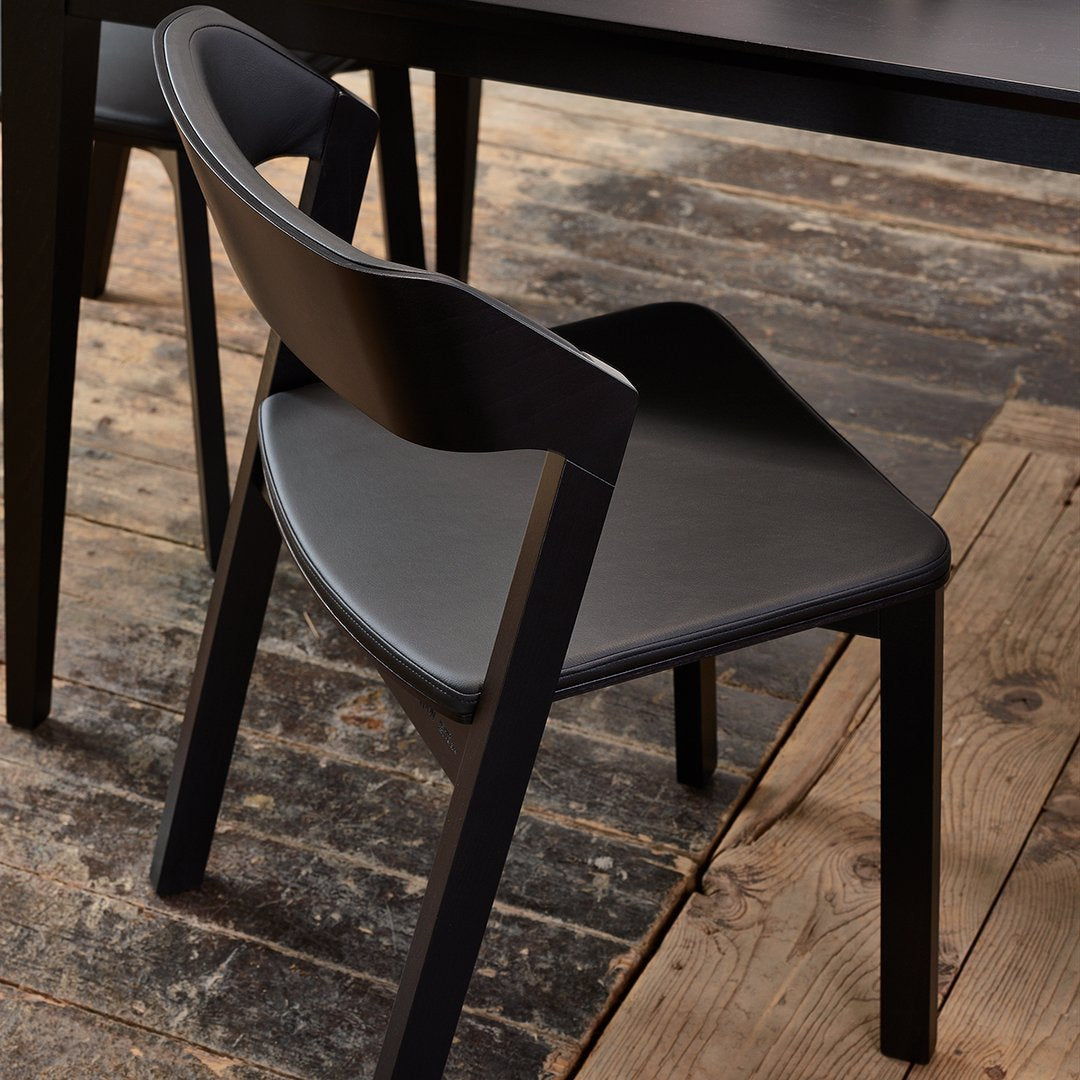Black wooden chair with a sleek design, featuring smooth, matte surfaces and clean lines against a rustic wooden floor.