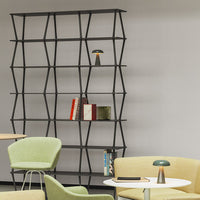 Black geometric bookshelf with green accent chairs and a modern lamp, featuring a minimalist design and light color palette.