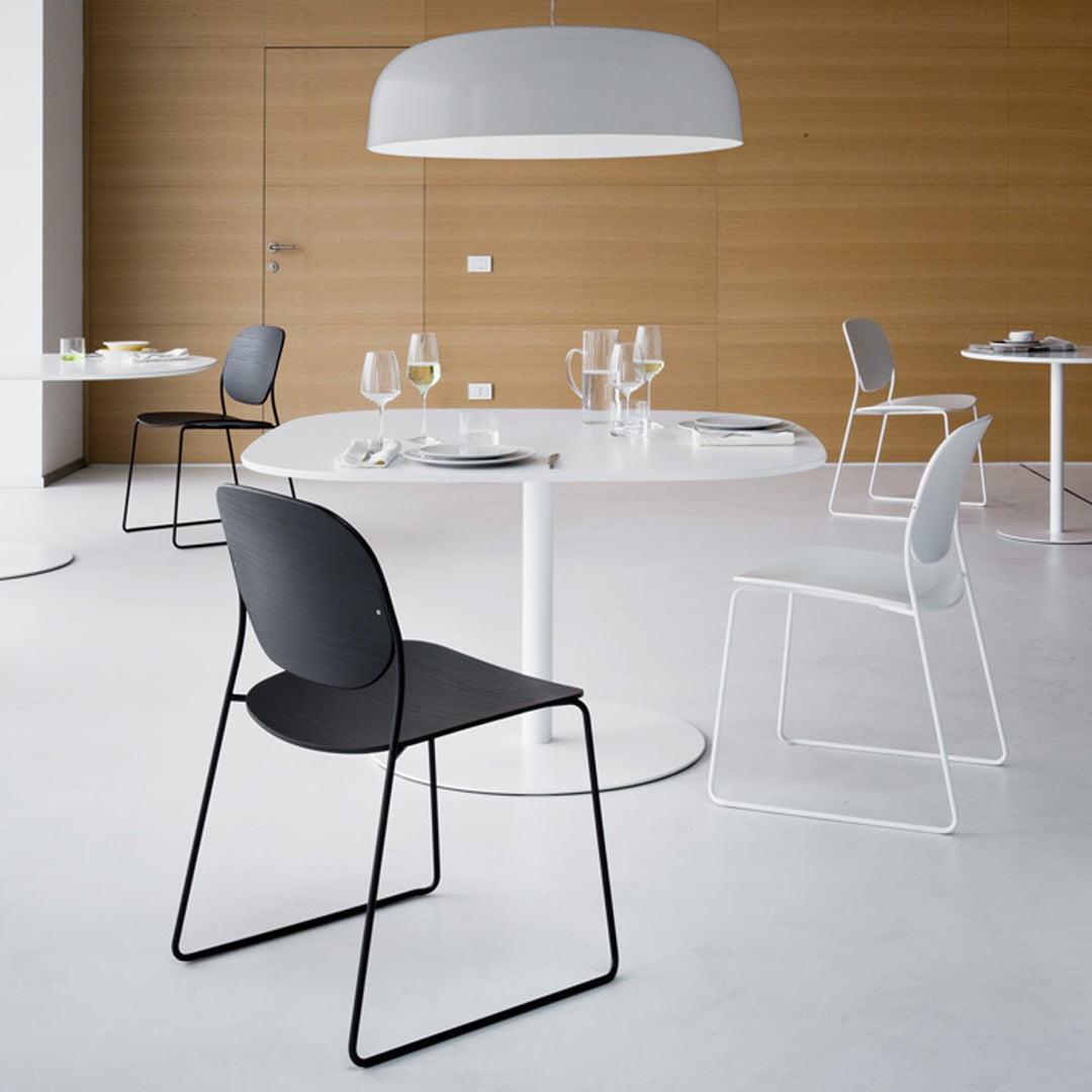 Modern dining chairs in black, white, and gray, set against a warm wood backdrop and a round white table.