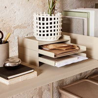 Beige desk organizer with layered drawers, paired with a white woven planter and neutral-toned stationery on a textured surface.