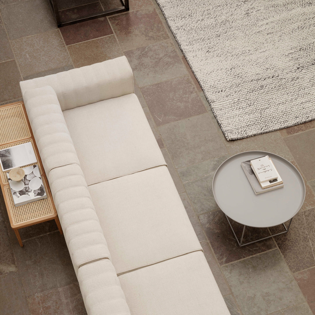 Neutral beige sofa with subtle ribbed texture, paired with a round gray table on a patterned stone floor.