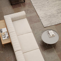Neutral beige sofa with subtle ribbed texture, paired with a round gray table on a patterned stone floor.